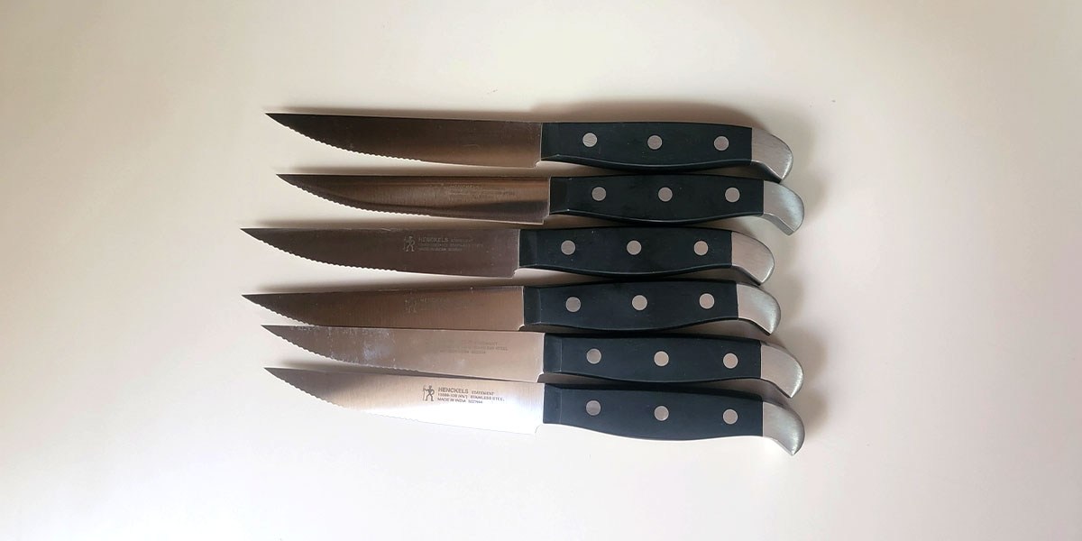 Six Henckels knives with black handles displayed horizontally Six Henckels knives with black handles displayed horizontally